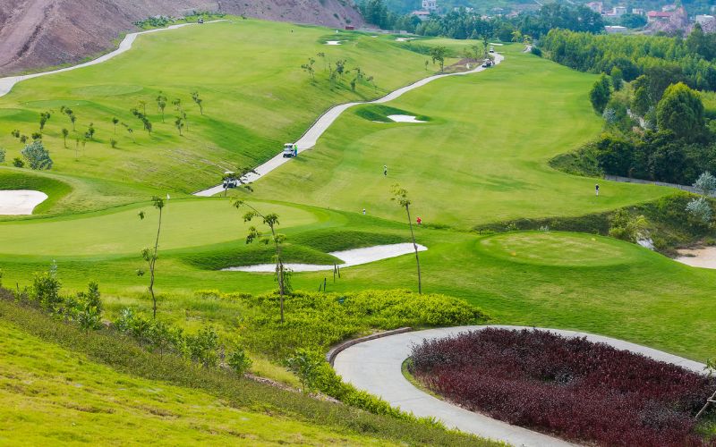 Aerial view of Amber Hills Golf Resort showing rolling green fairways, sand bunkers, and winding cart paths across the scenic hillside golf course in Vietnam.