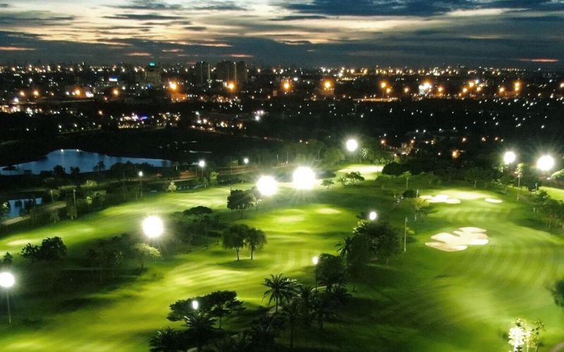 Night view of the floodlit fairways and greens at Panya Indra Golf Club in Bangkok, with the city skyline glowing in the background.