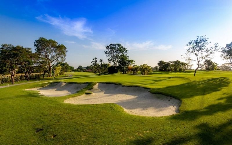 Sunny view of Tanah Merah Country Club fairway in Singapore with sand bunkers, lush greens, and scattered trees under a clear sky
