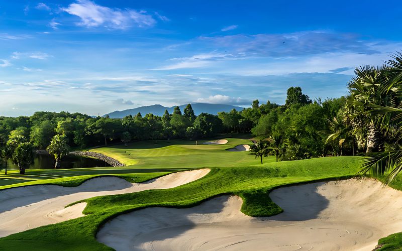 Scenic view of Amata Spring Country Club, featuring lush green fairways, several sand traps, and a clear blue sky, highlighting the beauty and challenge of the golf course layout.
