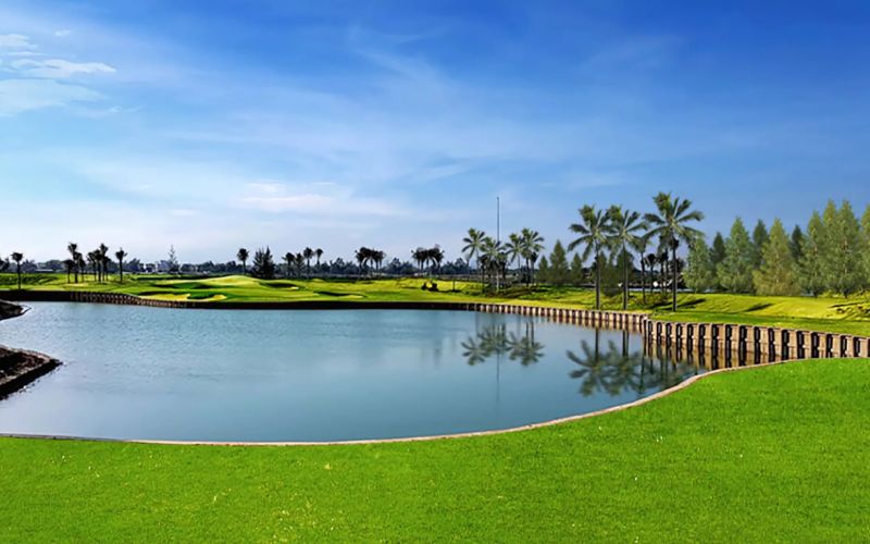 BRG Danang Golf Resort with a large reflective water feature, manicured fairways, and palm trees under a blue sky