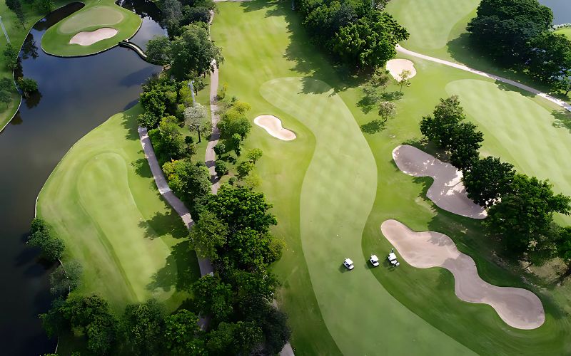 Aerial view of Bangkok Golf Club, showcasing well-manicured green fairways, strategically placed sand traps, and winding water features, creating a picturesque and challenging golf course layout.