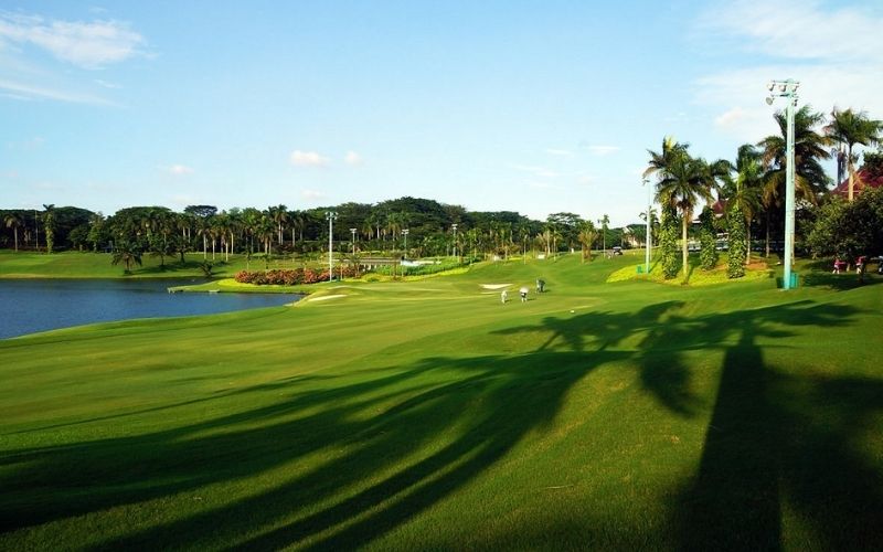 Scenic view of Damai Indah Golf course with well-manicured fairways, palm trees, and a water hazard under a clear blue sky.