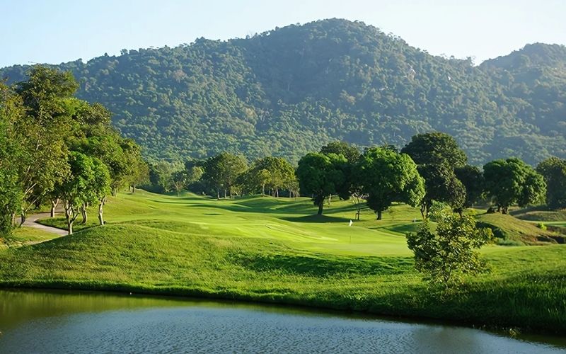 Scenic view of a golf course with lush green grass, a water feature, and rolling hills in the background.