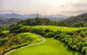 Panoramic view of FLC Ha Long Bay Golf Club with rolling fairways, lush greenery, and surrounding mountains overlooking Ha Long Bay.