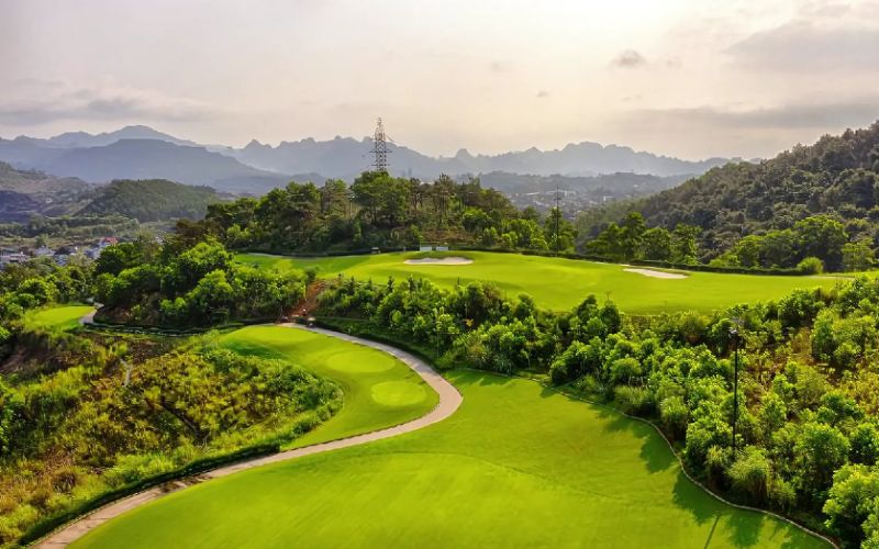 Panoramic view of FLC Ha Long Bay Golf Club with rolling fairways, lush greenery, and surrounding mountains overlooking Ha Long Bay.
