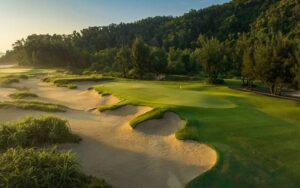 Golf course at Laguna Golf Lang Co with sandy bunkers, green fairways, and forested hills in the background.