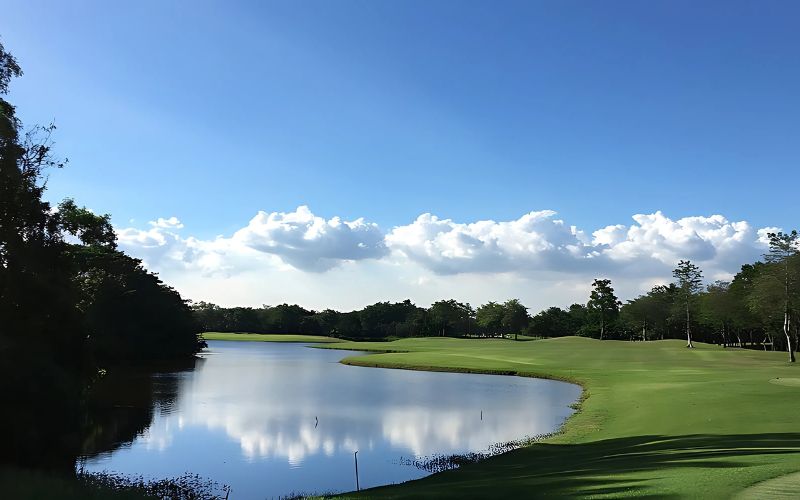 Scenic view of a golf course at Navatanee Golf Club, featuring a calm water hazard reflecting a partly cloudy sky, surrounded by lush green fairways and trees.