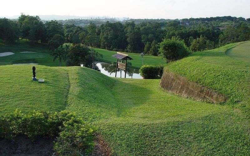 PT Badak NGL Golf Course with rolling green fairways, a small pond, and surrounding trees under a clear sky.