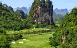 Green golf course surrounded by dramatic limestone mountains and lush vegetation at Phoenix Golf Resort in Vietnam.