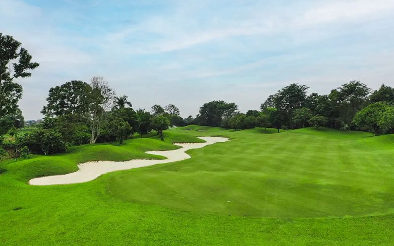 Wide fairway at Royal Sumatra Golf and Country Club with neatly trimmed grass, sand bunkers, and trees lining the horizon under a blue sky.