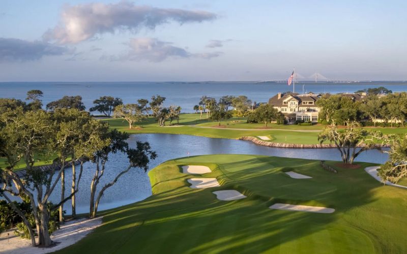 A picturesque view of the Sea Island Golf Club on Saint Simons Island, Georgia, featuring manicured greens, sand bunkers, coastal trees, and an ocean backdrop at sunset.
