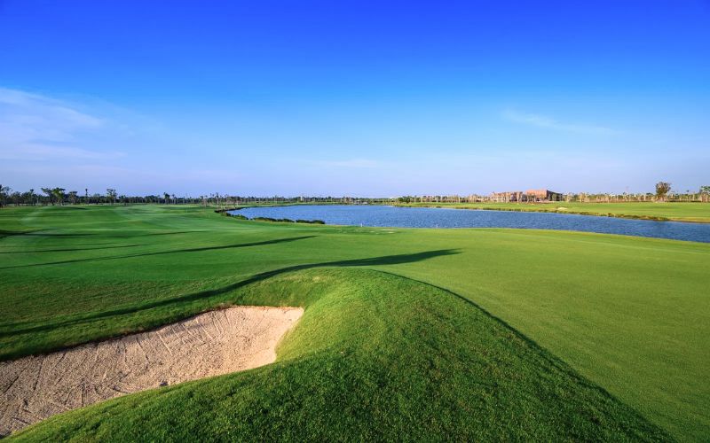 Wide view of Siam Country Club golf course in Bangkok featuring a green fairway, sand bunker, and clear blue sky.
