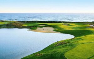 Coastal view of Vung Tau Paradise Golf Course with lush green fairways, sandy bunkers, and the ocean in the background under a clear sky.