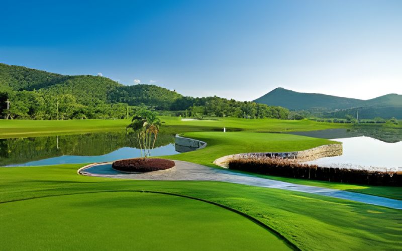 Beautiful view of Alpine Golf Resort Chiang Mai, Thailand, surrounded by green hills and a lake under clear blue skies.