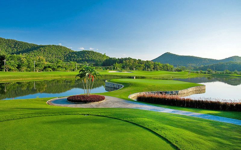 Alpine Golf Resort with lush green fairways, water hazards, and mountain views under a bright blue sky.