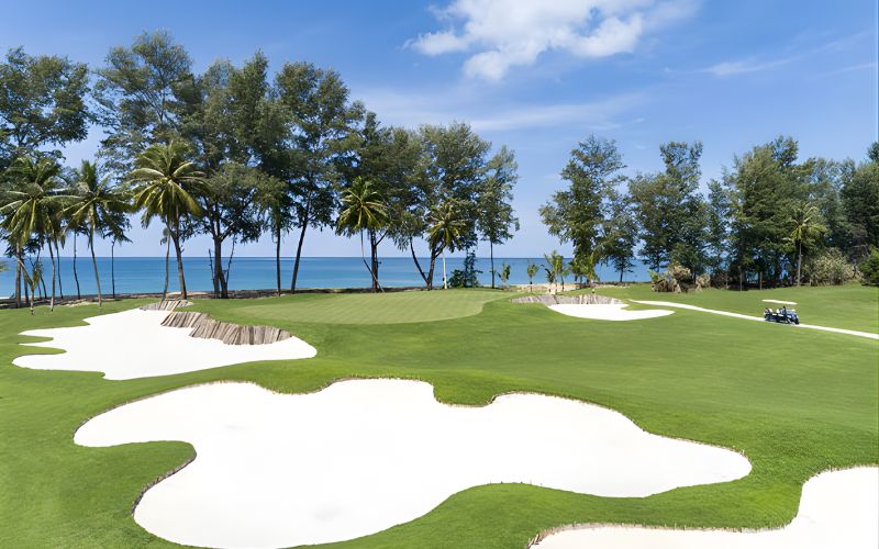 Aquella Golf Resort & Country Club featuring lush green fairways, white sand bunkers, palm trees, and an ocean view under a clear blue sky.