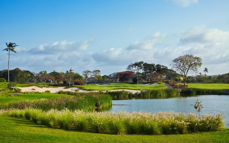 Scenic view of Bali National Golf Club with lush green fairways, water hazards, and blue sky in Nusa Dua, Bali.