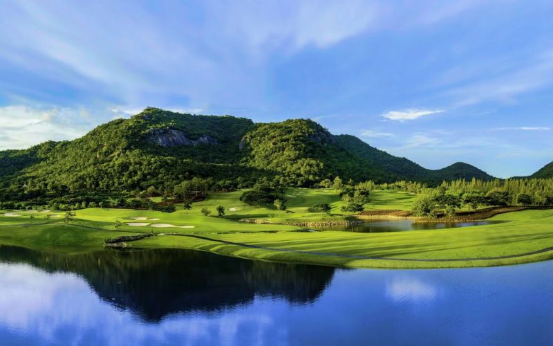 Scenic golf course with green fairways, a reflective water feature, and lush mountains under a clear blue sky at Black Mountain Golf Club.