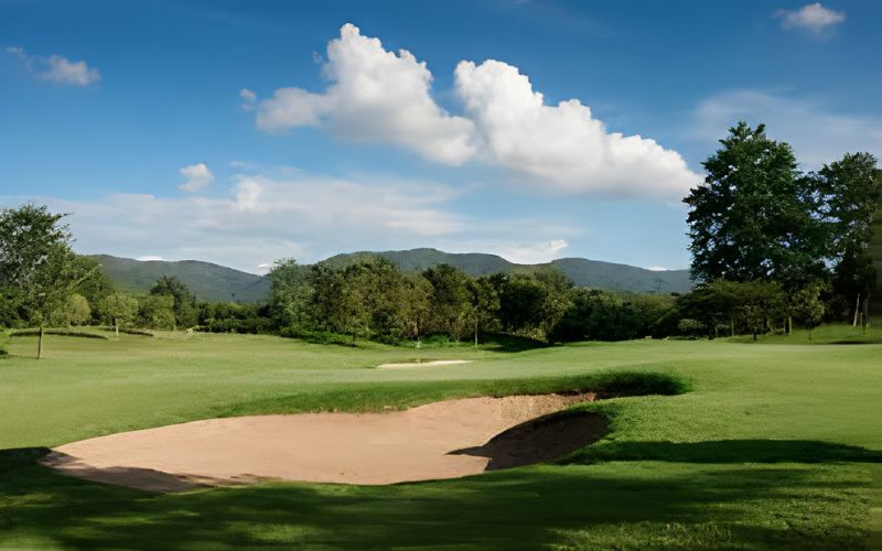 Beautiful fairway and sand bunker at Chiang Mai Highlands Golf & Spa Resort, surrounded by lush mountains and clear blue skies.