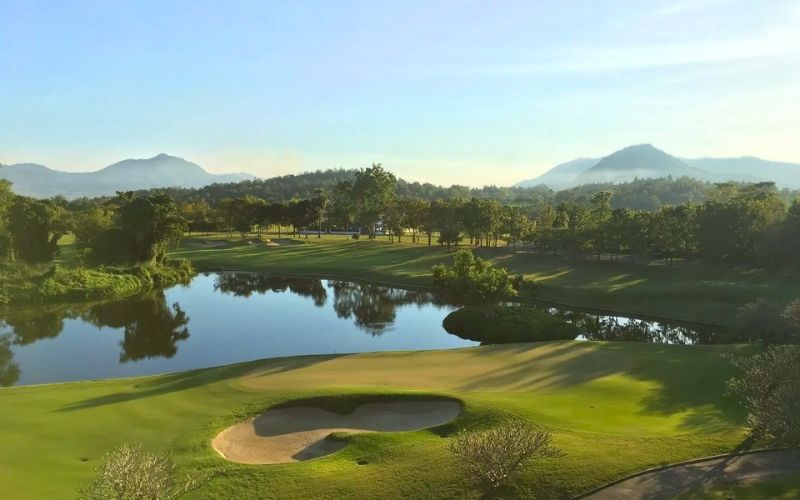 Chiang Mai Highlands Golf and Spa Resort surrounded by mountains, green fairways, and water features under a clear sky in northern Thailand.