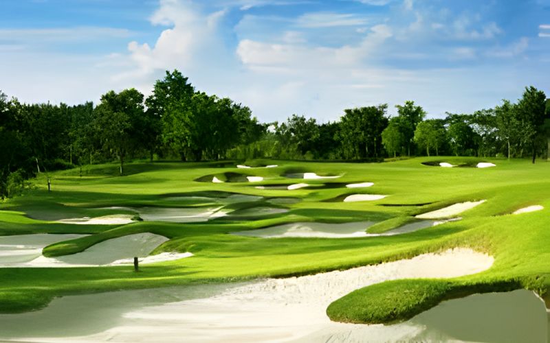 Beautiful golf course with sand bunkers and vibrant green fairways surrounded by trees under a bright blue sky at Chiang Mai Highlands Golf Spa Resort.