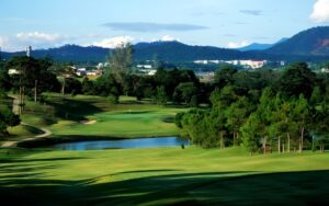 Scenic view of Dalat Palace Golf Club surrounded by pine trees, rolling hills, and mountain landscapes under a clear blue sky.
