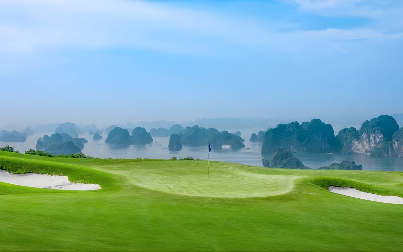 Morning view of FLC Ha Long Golf Club featuring lush green fairways overlooking Ha Long Bay’s limestone karsts under a misty blue sky.