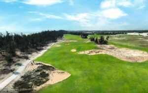 Golden Sands Golf Resort with expansive green fairways, sand bunkers, and a backdrop of trees along the coastline under a bright blue sky.