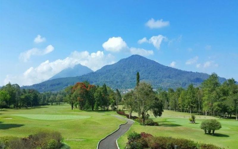 Handara Golf Resort Bali with lush green fairways, tall trees, and a mountain backdrop under a bright blue sky.