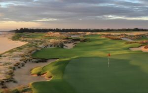 Sunset view of Hoiana Shores Golf Club showcasing coastal fairways, golden sand dunes, and the sea in the distance.