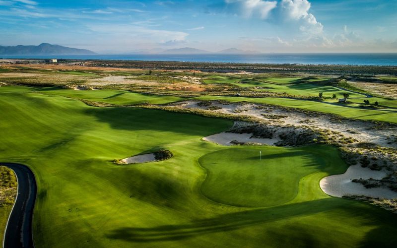 Aerial view of KN Golf Links in Cam Ranh featuring rolling fairways, sand dunes, and ocean views under a bright blue sky.