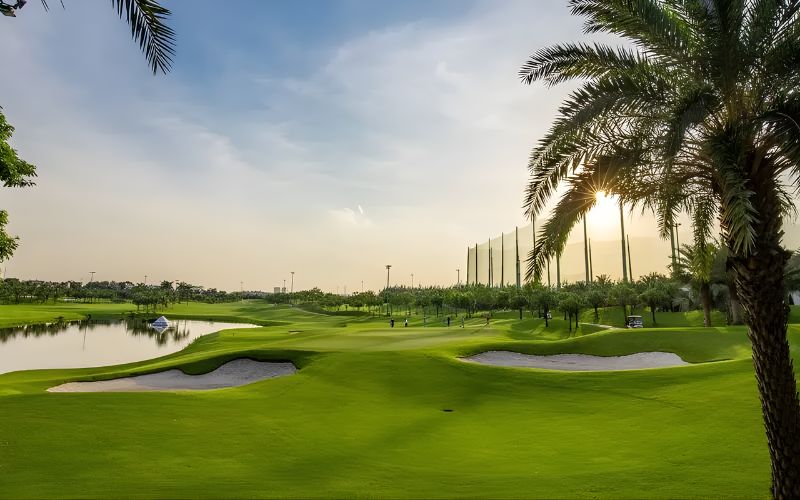 Long Bien Golf Club at sunset with palm trees, green fairways, and soft golden light over the course.