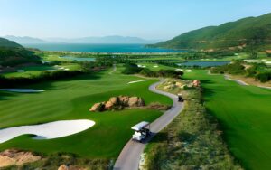Aerial view of Montgomerie Links Vietnam with rolling fairways, mountain backdrop, and coastal scenery.