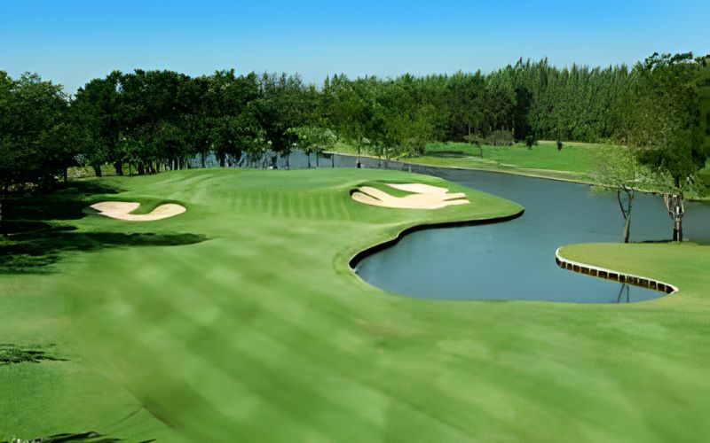 View of Muang Kaew Golf Club in Thailand, featuring lush fairways, water hazards, and sand bunkers surrounded by tall trees under a clear blue sky.