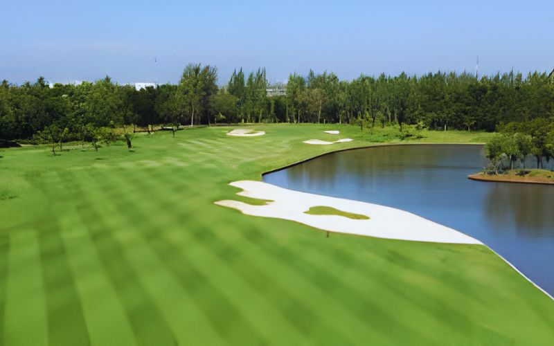 Muang Kaew Golf Course in Bangkok featuring green fairways, white sand bunkers, and a calm lake under a bright sky.