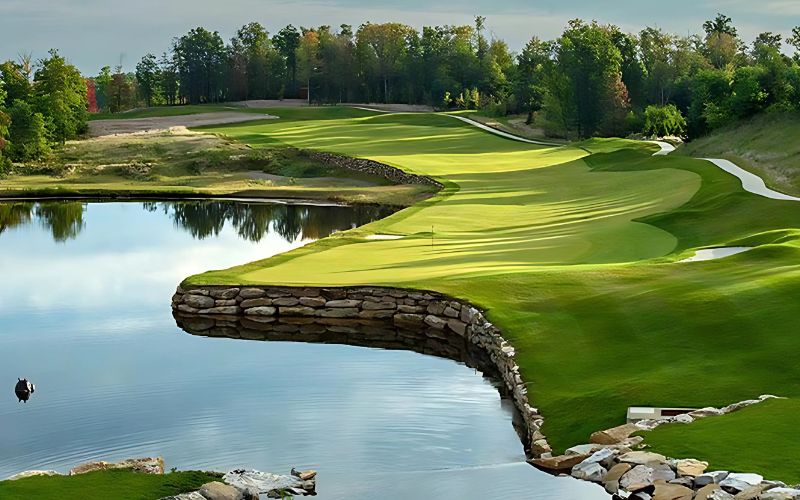 Scenic view of PGA NovaWorld Phan Thiet Golf Course with a stone wall lining the water hazard, lush green fairways, and trees in the background
