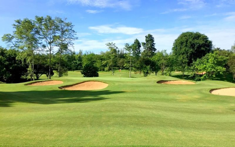 Royal Chiang Mai Golf Resort featuring a bright green fairway with sand bunkers, surrounded by tropical trees and lush vegetation under a clear blue sky