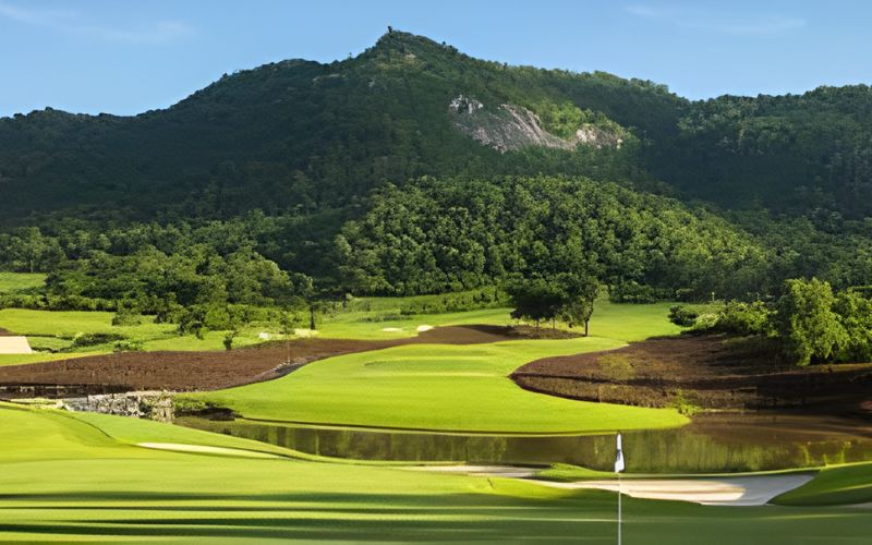 Scenic view of Royal Hua Hin Golf Course in Thailand, surrounded by lush greenery and mountain backdrops under a clear blue sky.