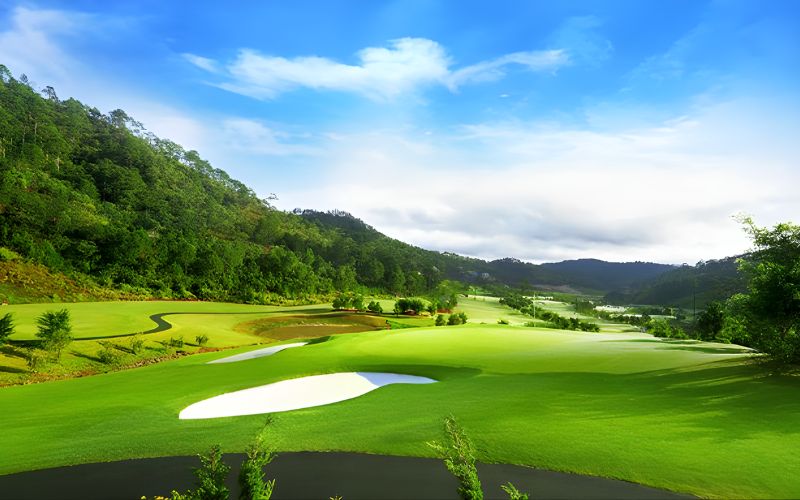 Sunny view of SAM Tuyen Lam Golf Course surrounded by pine-covered hills and calm blue skies.