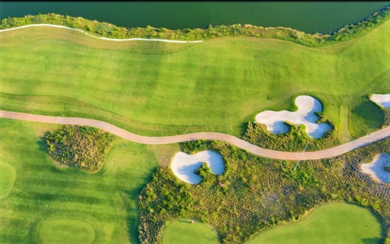 Aerial view of Sedayu Indo Golf course with lush green fairways, sand bunkers, water hazards, and a winding pathway.