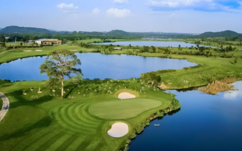 Aerial view of Siam Country Club Pattaya golf course, showing green fairways, sand bunkers, and water hazards under a clear blue sky.