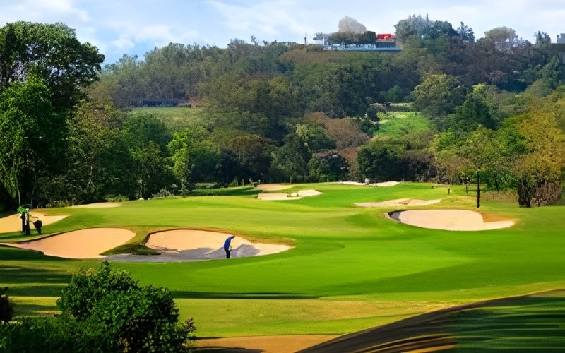 Scenic view of Siam Country Club golf course with manicured fairways, sand bunkers, and lush trees surrounding the landscape under a bright sky.