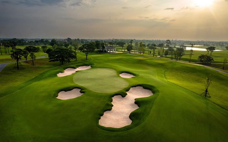 Aerial view of Stonehill Golf Club with neatly trimmed fairways, several sand bunkers, and a soft golden sky in the background