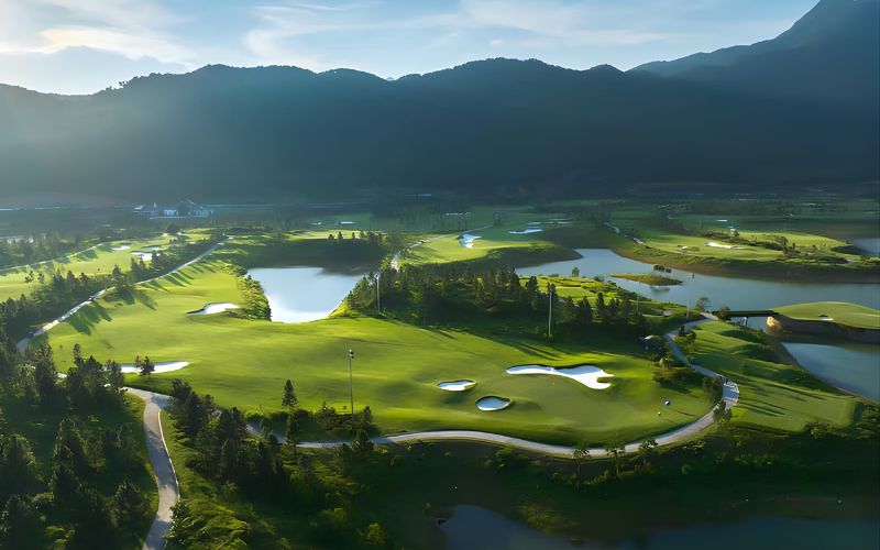 Aerial view of Thanh Lanh Valley Golf Resort surrounded by lakes, rolling hills, and lush greenery under soft sunlight.