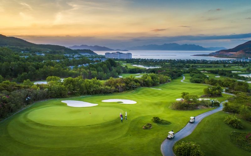 Scenic view of Vinpearl Golf Phu Quoc featuring lush green fairways, surrounding hills, and a coastal backdrop at sunset.