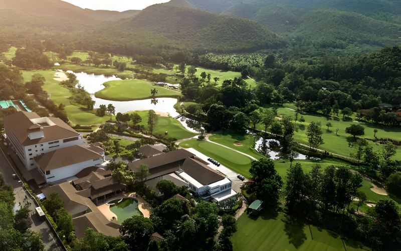 Aerial view of Alpine Golf Course Resort with green fairways, surrounding trees, and distant mountain landscape under warm sunlight.