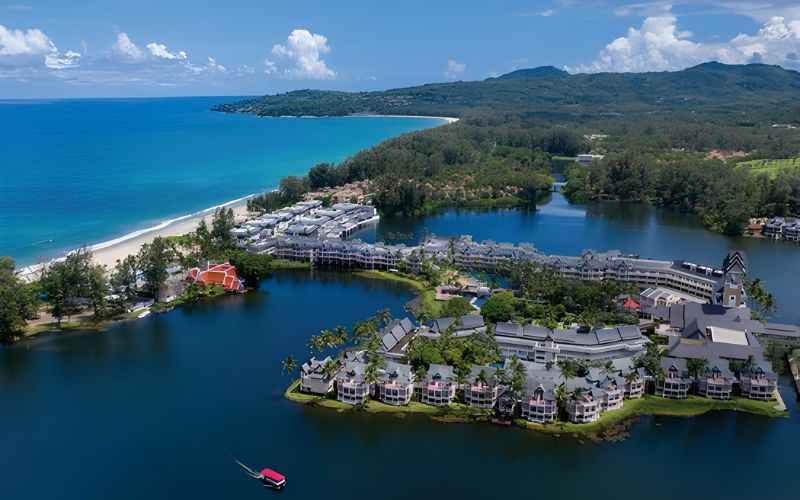 Aerial view of Angsana Laguna Phuket resort surrounded by turquoise lagoons, tropical greenery, and the Andaman Sea coastline under a clear blue sky.