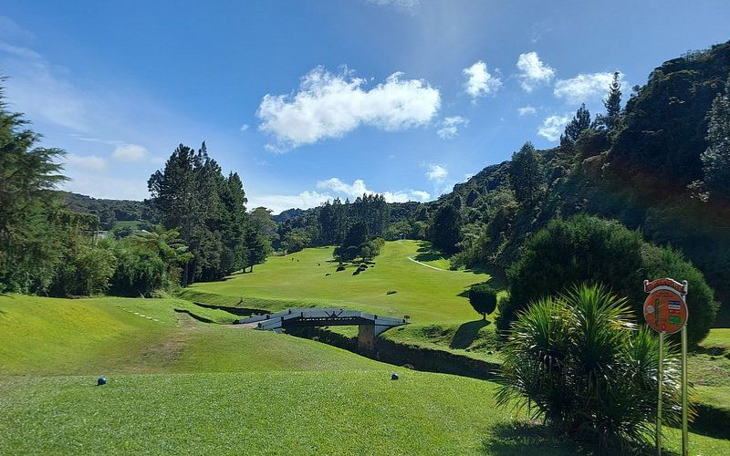 Sunny day view of Cameron Highlands Golf Club with green fairways, rolling hills, and lush trees under a blue sky with clouds.