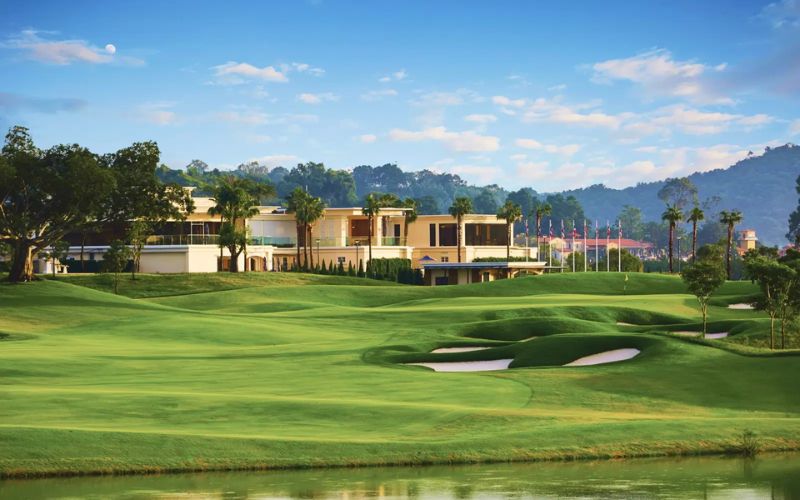 Scenic view of Chee Chan Golf Resort in Pattaya, Thailand, featuring a well-manicured fairway, modern clubhouse, and mountain backdrop under a bright blue sky.